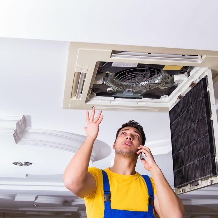 HVAC technician inspecting ceiling air conditioner for maintenance issues