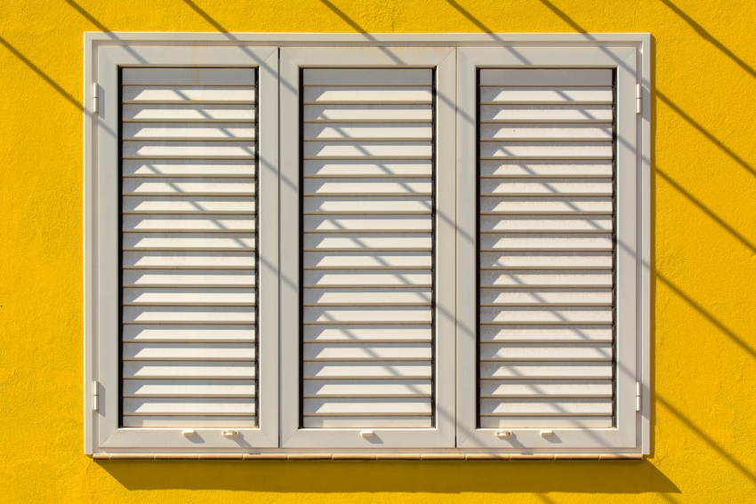 White louvered window shutters on bright yellow exterior wall
